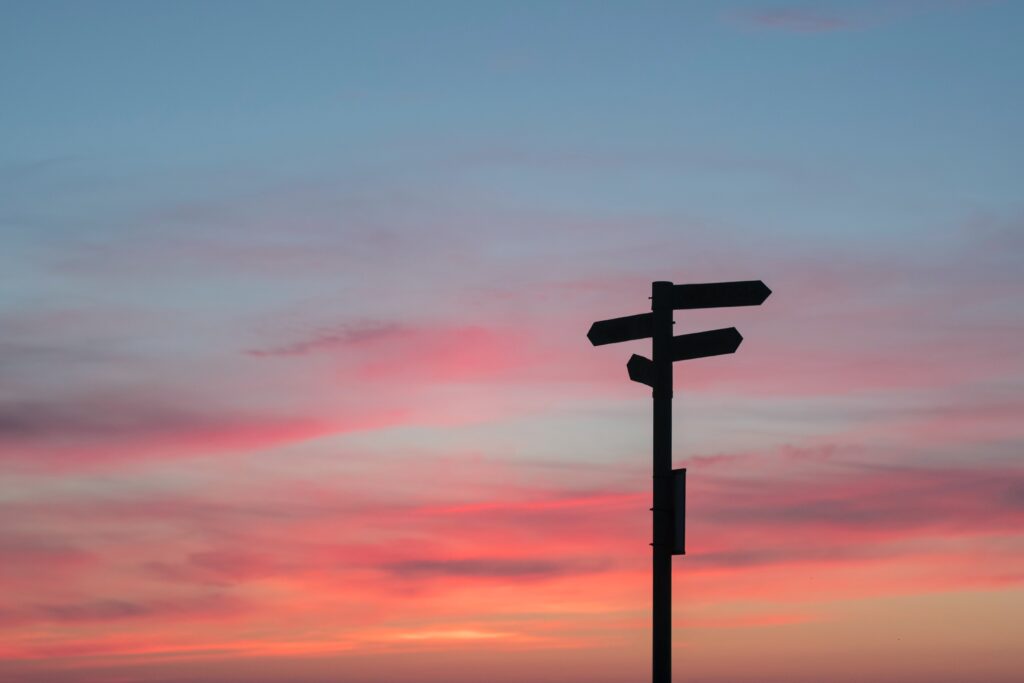 a photo of a signpost set against a pink and orange sunset sky