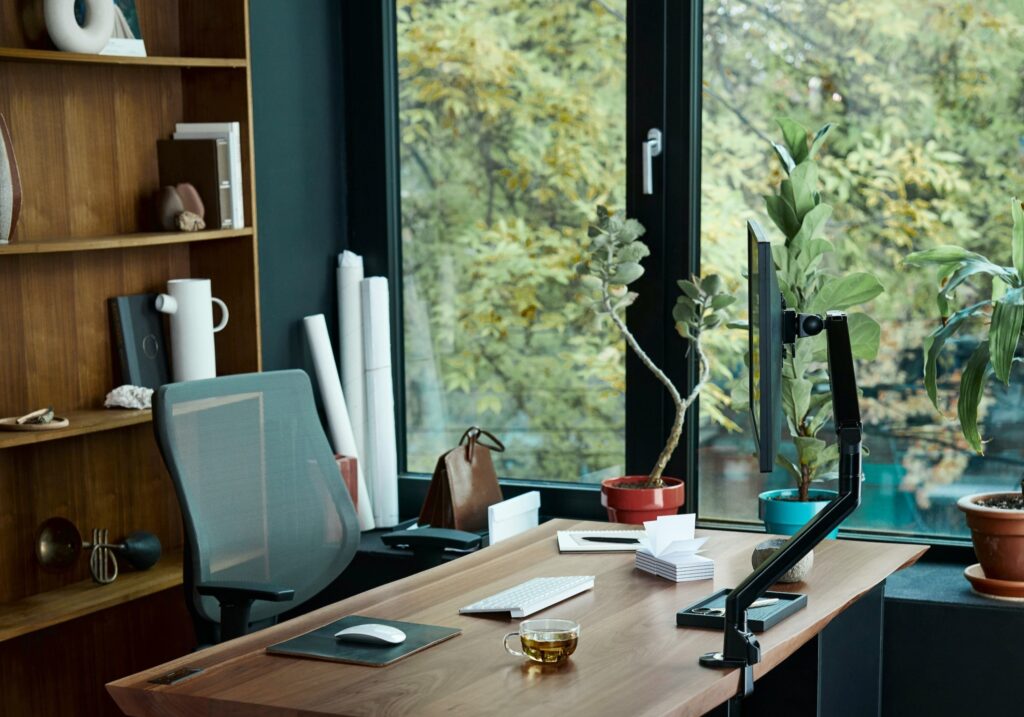 an image of a desk setup at home, next to tall windows looking out over trees