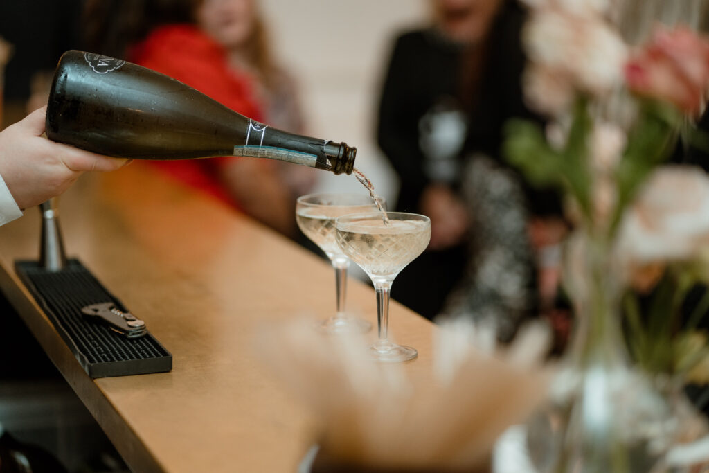 someone pouring champagne from a bottle into two coupe glasses