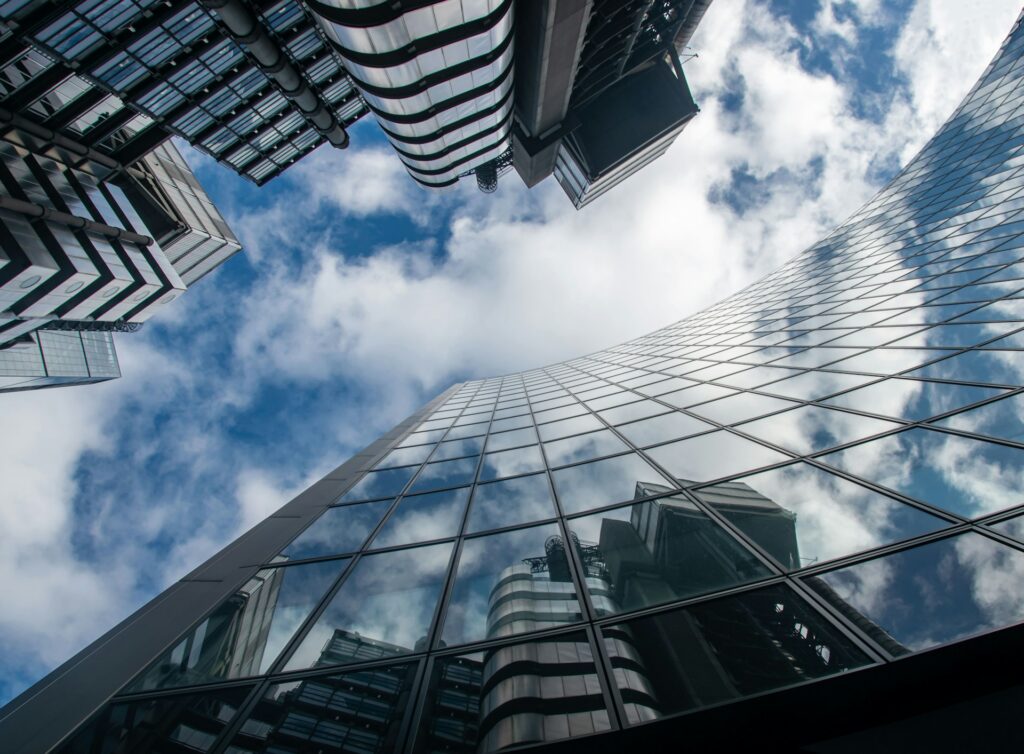 image looking upwards towards a blue and cloudy sky between two large glass building