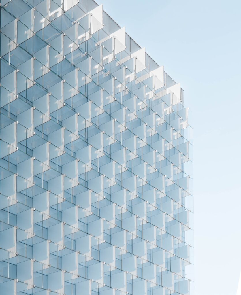 an image of an architectural office building made of glass, taken at an upwards angle against a blue sky