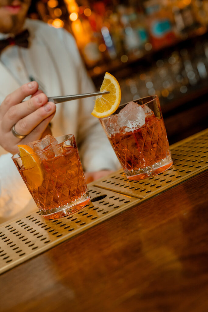 A photograph of a barman preparing two cocktails.