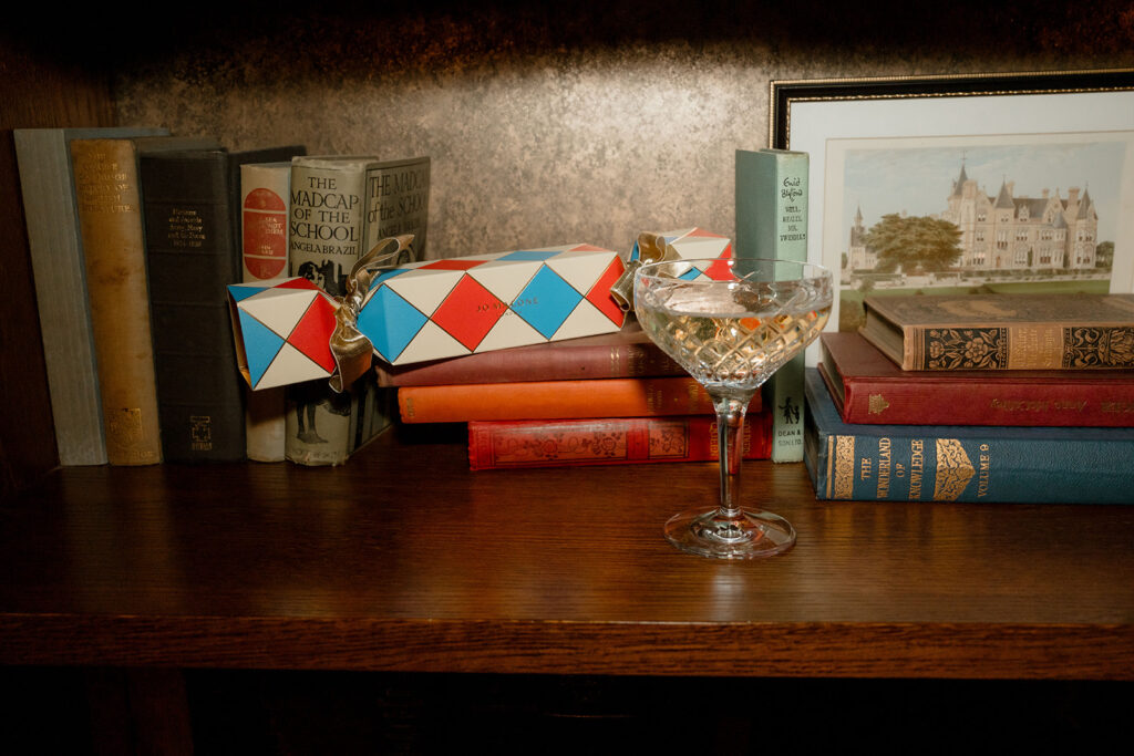 A photograph of a glass of champagne and a Christmas cracker gift placed on a bookshelf.