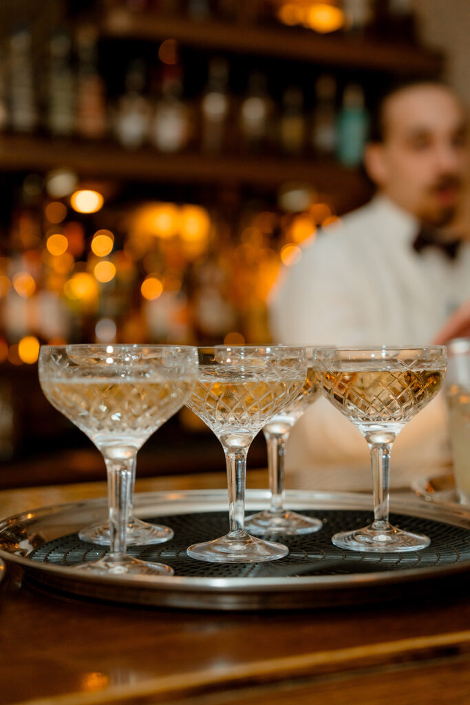 A photograph of four glasses of champagne on a tray, positioned atop a bar.