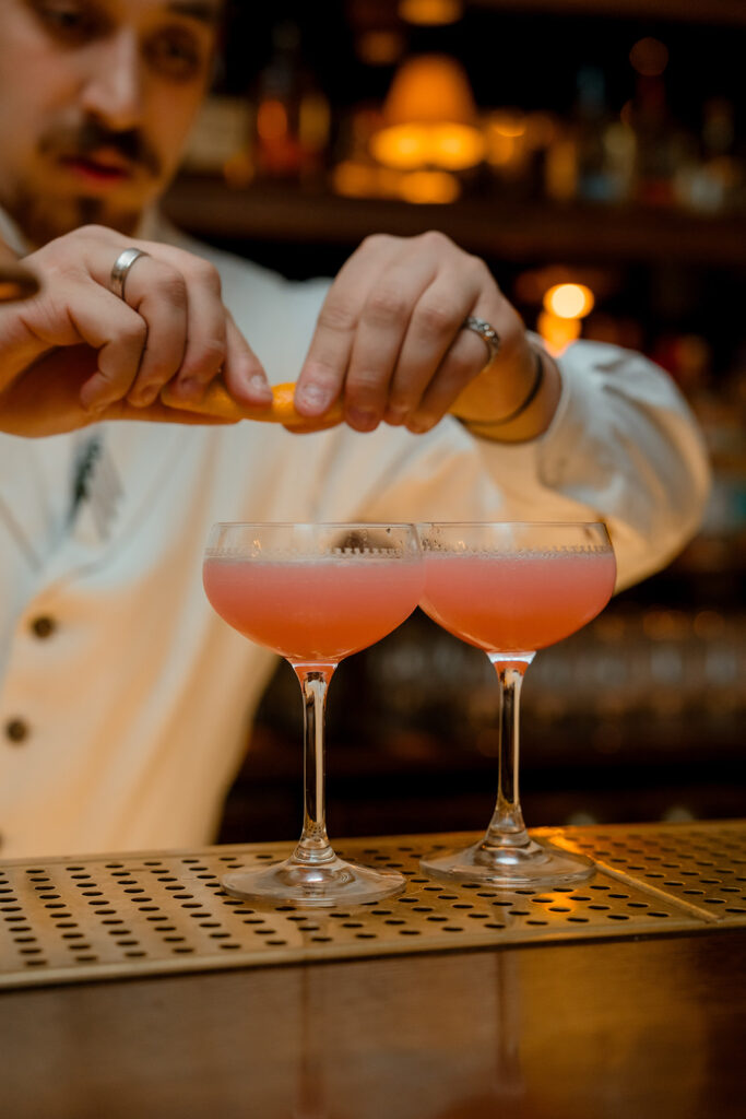 A photograph of a barman preparing two cocktails.